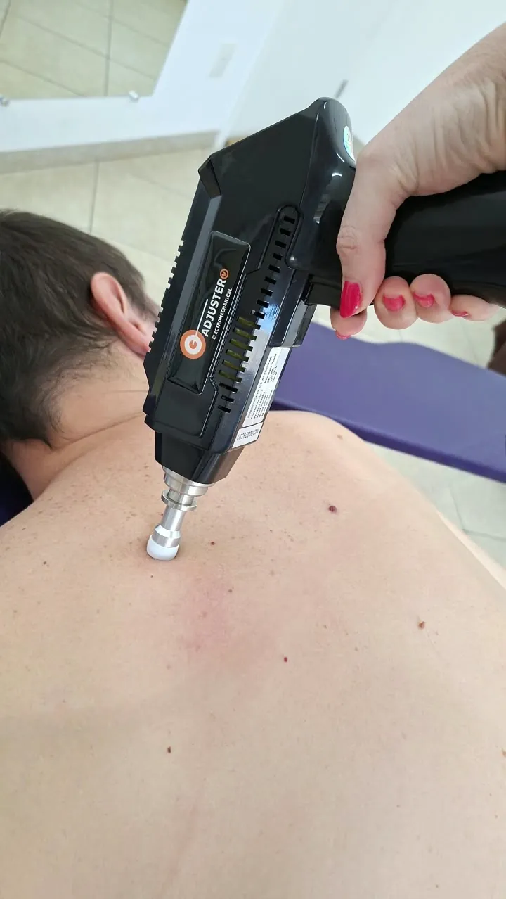 Dra. Gisela aplicando o aparelho Adjuster nas costas de um paciente deitado na maca