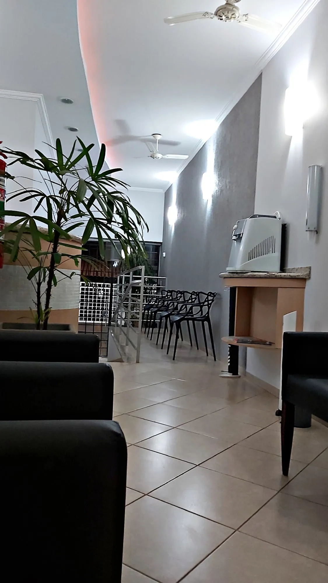 Recepção do consultório, com poltronas escuras, cadeiras e plantas